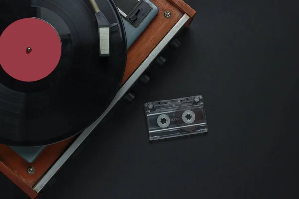 Retro music concept. Vinyl record player with a vinyl record, audio cassette on a black background. 80s. Top view
