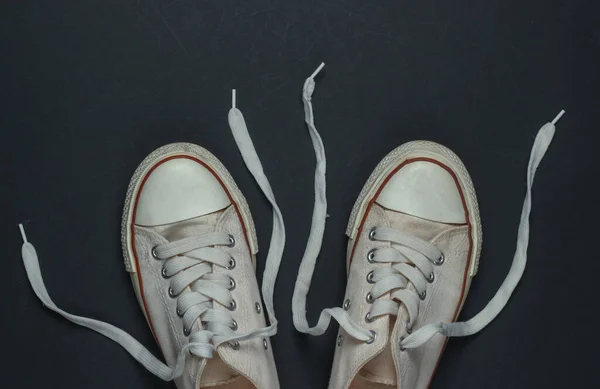 White old sneakers with untied laces on a black background. Top view