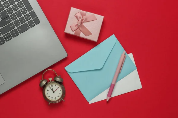 Laptop, alarm clock, santa letter envelope, gift boxes with bow on red background. 11:55 am. New Year, Christmas concept. Top view