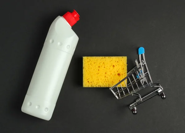 Cleaning concept. Shopping trolley with detergent bottle, sponge on black background