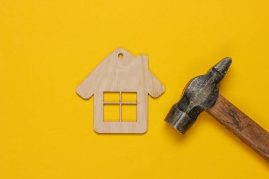 Bir ev nasıl inşa edilir? Diy konsepti. Sarı arka planda çekiç ve mini ev figürleri