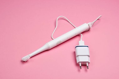 Pembe pastel arka planda şarj aleti olan modern elektrikli diş fırçası..