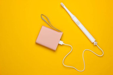Sarı arka planda elektrik bankasıyla şarj olan modern elektrikli diş fırçası. Üst görünüm