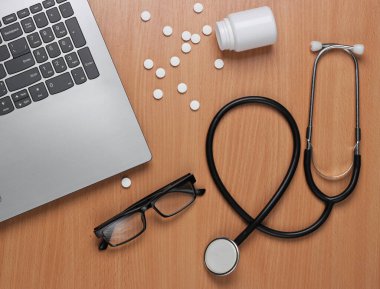 Doktorun çalışma alanı. Ofis masasında bir şişe hap, dizüstü bilgisayar ve steteskop var. Üst görünüm