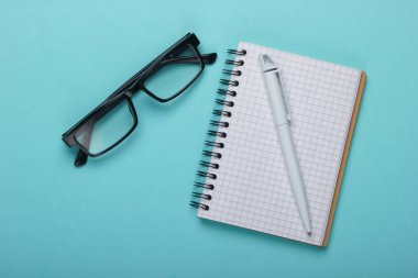 Klasik gözlük ve mavi pastel arka planda kalemli defter. Üst görünüm