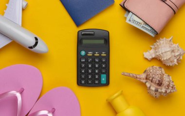 Dinlenmenin maliyetinin hesaplanması. Yaz dönemi. Gezgin, plaj aksesuarları, oyuncak uçak, sarı arka planda hesap makinesi. Üst görünüm.