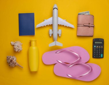 Dinlenmenin maliyetinin hesaplanması. Yaz dönemi. Gezgin, plaj aksesuarları, oyuncak uçak, sarı arka planda hesap makinesi. Üst görünüm.