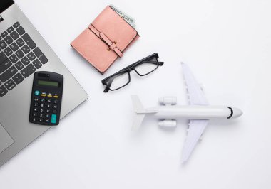 Hava ulaşımı, uçuş veya seyahat maliyetinin hesaplanması. Laptop, hesap makinesi, cüzdan, gözlük, beyaz arka planda oyuncak uçak. Üst görünüm