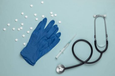 Doktor aletleri mavi arka planda. Eldivenler, şırınga, steteskop ve haplar. Üst görünüm