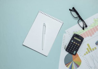Ekonomik analiz, istatistik, analitik. Hesap makinesi, gözlük ve defter, mavi arkaplanda grafikler ve çizelgeler. Üst görünüm
