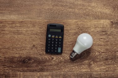 Ahşap zeminde hesap makinesi ve ampul. Ekonomi, ekonomi kavramı. Paranı kendine sakla. Üst görünüm