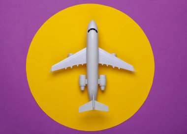 Mor arka planda sarı daireli uçağın oyuncak modeli. Turizm, hava yolculuğu, minimalizm. Üst görünüm