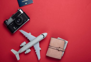Kırmızı arka planda düz seyahat kompozisyonu. Uçak figürü, pasaport, içinde dolar olan cüzdan, kamera. Eğlence, tatil ve turizm, minimalizm konsepti. Üst görünüm