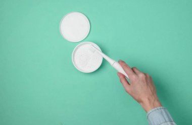 Kadın eli mavi arka planda modern bir elektro diş fırçası ve diş pudrası tutuyor. Üst görünüm