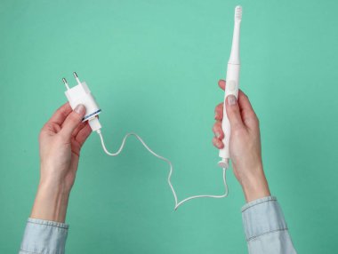 Kadın eli mavi arka planda şarj aleti olan modern bir elektro-diş fırçası tutuyor. Üst görünüm