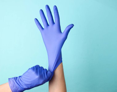 Doktorun elleri mavi arka planda lastik eldiven takıyor.