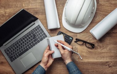 Mühendis çalışma alanı. Erkeklerin elleri iş yerinin arka planına bir defter yazar. Üst görünüm