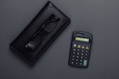 Siyah arka planda şık bir cüzdan, gözlük ve hesap makinesi. Üst görünüm