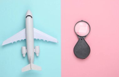 Düz seyahat kompozisyonu. Pembe pastel arka planda uçak figürü ve büyüteç. Üst Manzara. Minimalizm