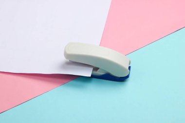 Zımba, mavi-pembe pastel arka plan üzerine beyaz bir kağıt parçası saplar..