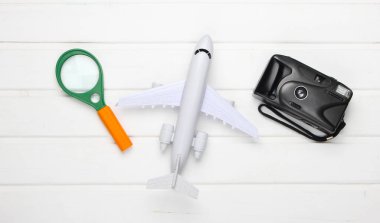 Uçak, kamera ve büyüteçle seyahat konseptinin düz dizaynı. Beyaz ahşap arka plan. Minimalizm. Üst görünüm