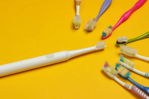 Modern electric toothbrush and old used toothbrushes on yellow background. Top view