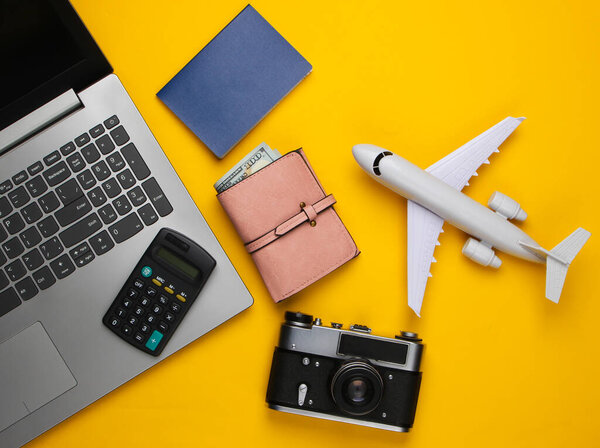 Calculation of the cost of rest or emigration, air flight. Travel background. Traveler, tourist accessories, laptop, toy airplane, passport, calculator on a yellow background. Top view.