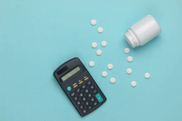 Economic calculation of the cost of treatment, analysis of the cost of medicines. Bottle of pills, calculator on blue background. Top view