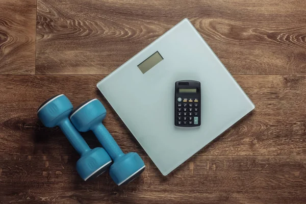 The concept of weight loss, fitness. Calorie Counting. Floor heights, calculator and dumbbells on a wooden floor. Top view