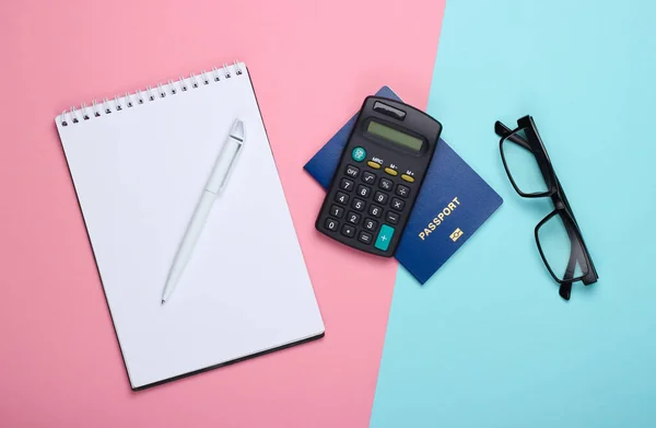 Flat lay economic  and travel composition. Calculator, notebook, glasses and passport on blue pink pastel background. Top view