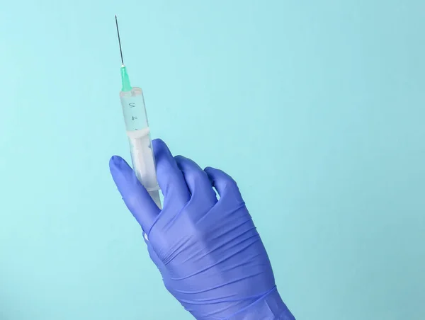 Doctor's hand in a glove holds a syringe with injection on a blue background. Vaccinations. Epidemic.