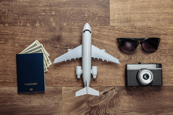 Travel flat lay composition. Plane figurine, camera, passport with dollar bills, sunglasses on wooden floor. Rest, vacation. Top view