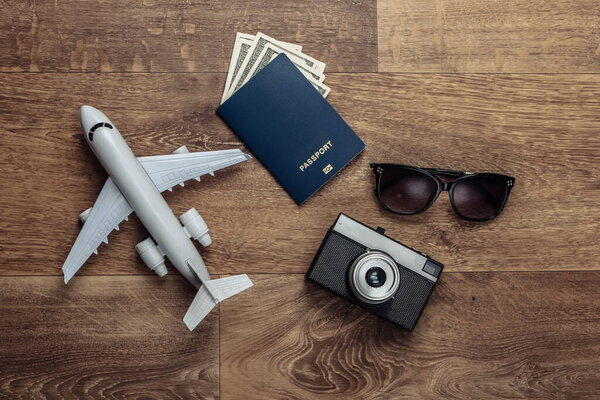 Travel flat lay composition. Plane figurine, camera, passport with dollar bills, sunglasses on wooden floor. Rest, vacation. Top view