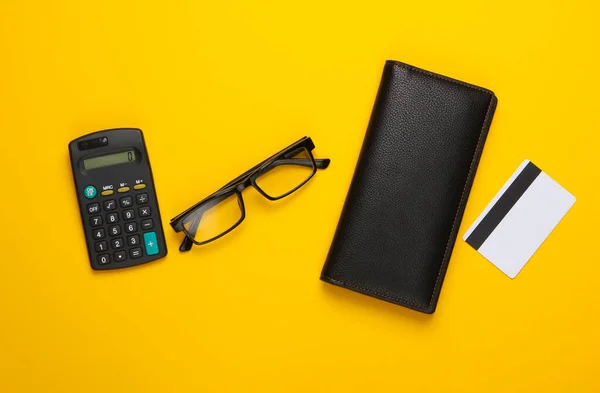 Calculation of the family budget, calculation of expenses. Wallet and bank card, calculator on yellow background. Top view