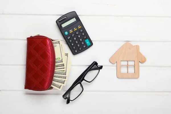 Calculation of rent payment for housing. Creative flat lay composition. House figurine, calculator, wallet with money on a white table. Top view