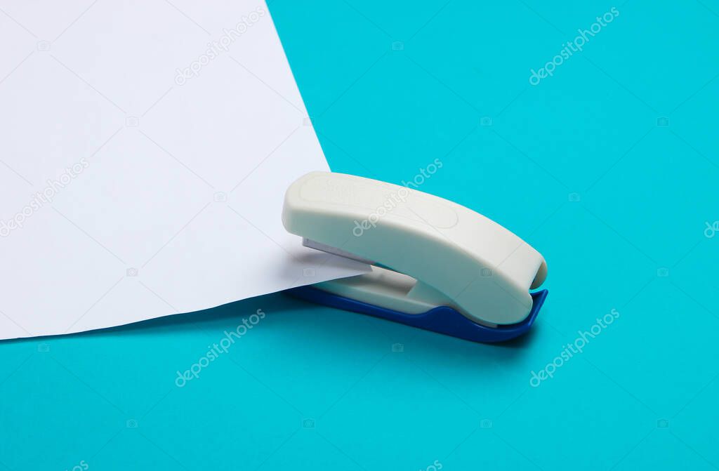Stapler stabs a white sheet of paper on blue background.