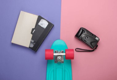 Yaz eğlencesi. Gençlik düzlüğü. Retro kameralı kruvazör tahtası, pembe arkaplanlı video kaset. Retro 80 'ler. Üst görünüm