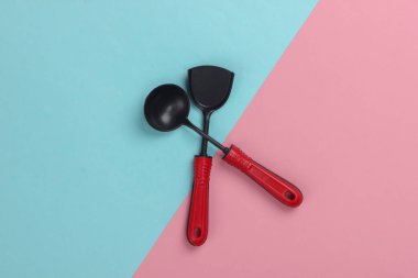 Pembe-mavi pastel arka planda oyuncak mutfak aletleri. Mutfak spatulası, kepçe. Üst görünüm
