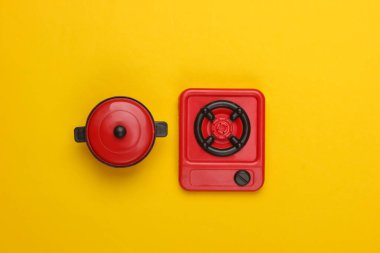 Sarı arka planda tavası olan oyuncak plastik soba. Çocuk Mutfağı. Üst görünüm, minimalizm