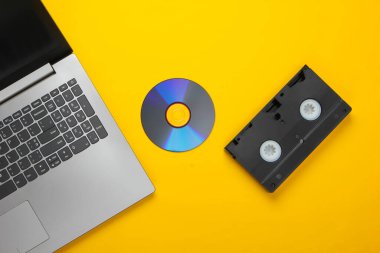 Düz dizüstü bilgisayar, CD disk, sarı arka planda ses kaseti. Retro depolama ortamı. Üst görünüm