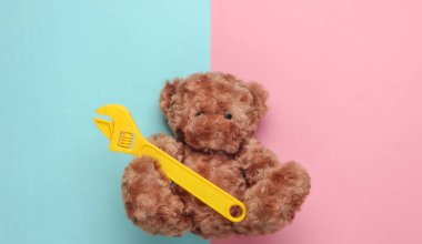 Oyuncak ayı mavi pembe renkli arka planda oyuncak anahtar tutuyor. Tamir konsepti. Üst görünüm