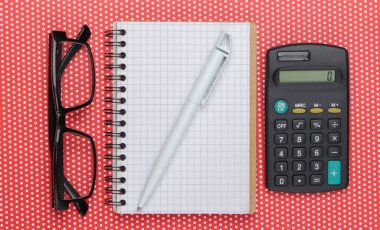 Kalem ve gözlüklü defter, puantiyeli masa örtüsü üzerinde hesap makinesi. Üst görünüm