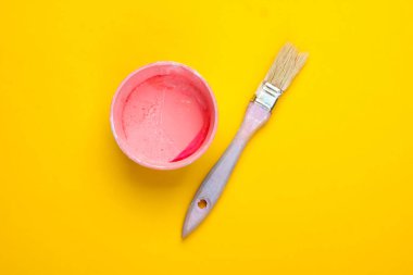İçinde boya olan boş bir kutu ve sarı arka planda bir fırça. Pastel renk eğilimi. Üst görünüm