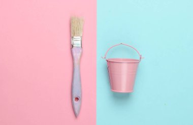 Pembe arka planda boş bir kova ve boya fırçası. Pastel renk eğilimi. Üst görünüm