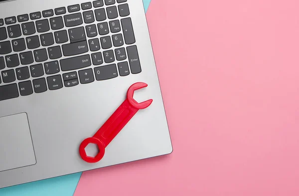 Flat lay composition. Repair concept. Laptop with toy wrench on pink blue pastel background. Top view