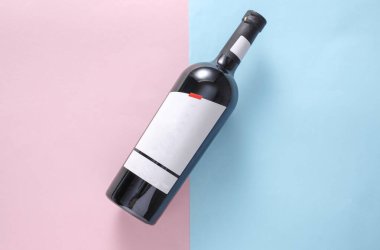 Bottle of red wine with white blank label on blue pink background