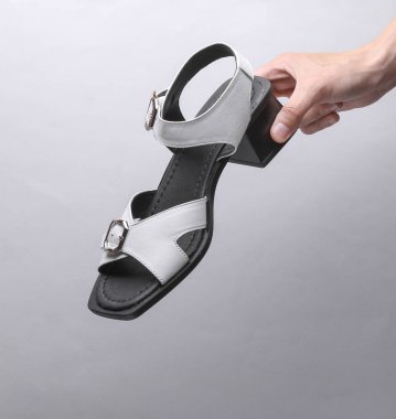 Female hand holding leather sandal on grey background