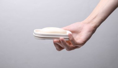 Hand holding soap dish with soap on grey background