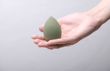 Female hand holding makeup sponge on gray background