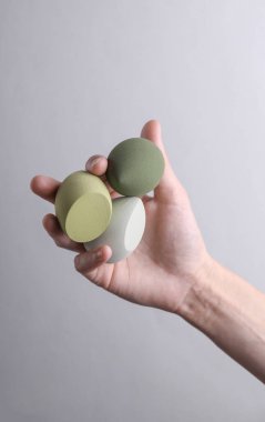 Female hand holding makeup sponges on gray background